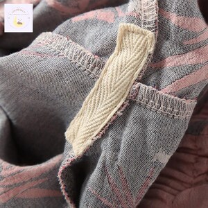 May include: Close-up of a gray fabric with pink and white striped patterns. A beige herringbone tape is sewn into the fabric. The stitching is visible, and the fabric appears to be soft and textured. The overall aesthetic is casual and comfortable.