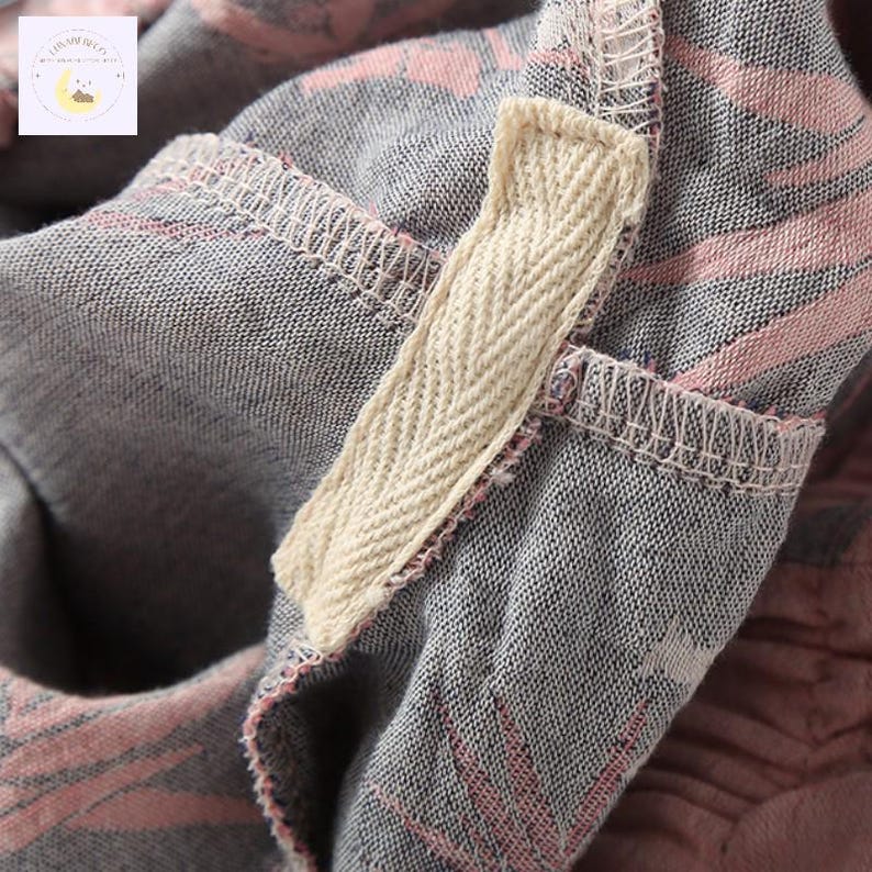 May include: Close-up of a gray fabric with pink and white striped patterns. A beige herringbone tape is sewn into the fabric. The stitching is visible, and the fabric appears to be soft and textured. The overall aesthetic is casual and comfortable.