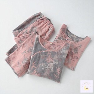 May include: A two-piece pajama set in pink and gray, featuring a floral and bamboo leaf pattern. The set includes a long-sleeved top with a wrap-style closure and matching pants. The fabric appears soft and lightweight, suitable for sleepwear.
