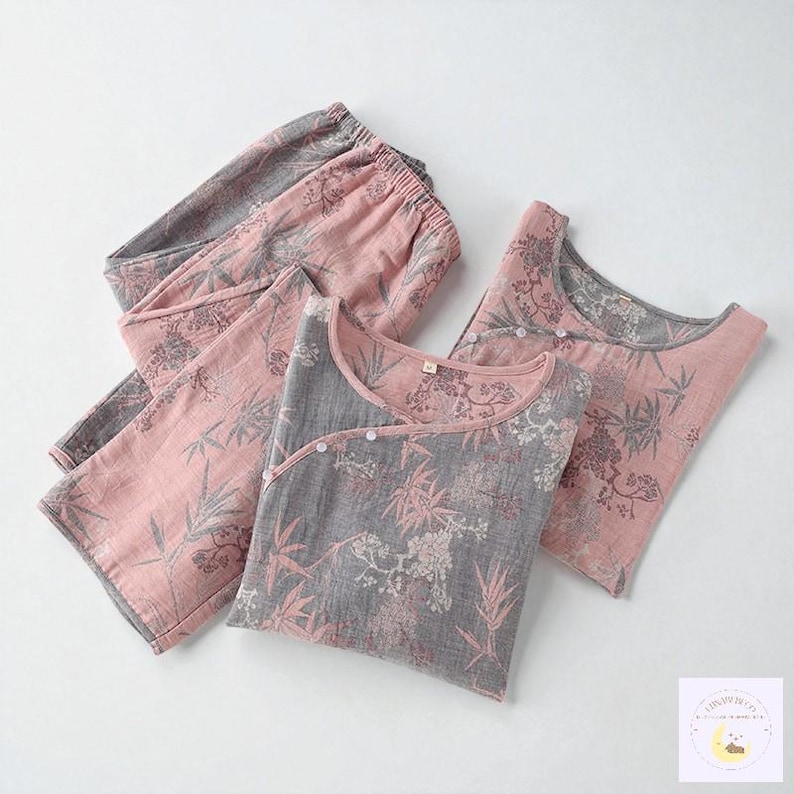 May include: A two-piece pajama set in pink and gray, featuring a floral and bamboo leaf pattern. The set includes a long-sleeved top with a wrap-style closure and matching pants. The fabric appears soft and lightweight, suitable for sleepwear.