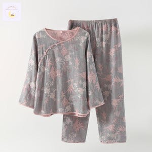 May include: Gray pajama set with a floral pattern in pink and white. The long-sleeved top has a wrap-style closure with buttons. The pants have an elastic waistband. The edges of the top and pants are trimmed in pink.