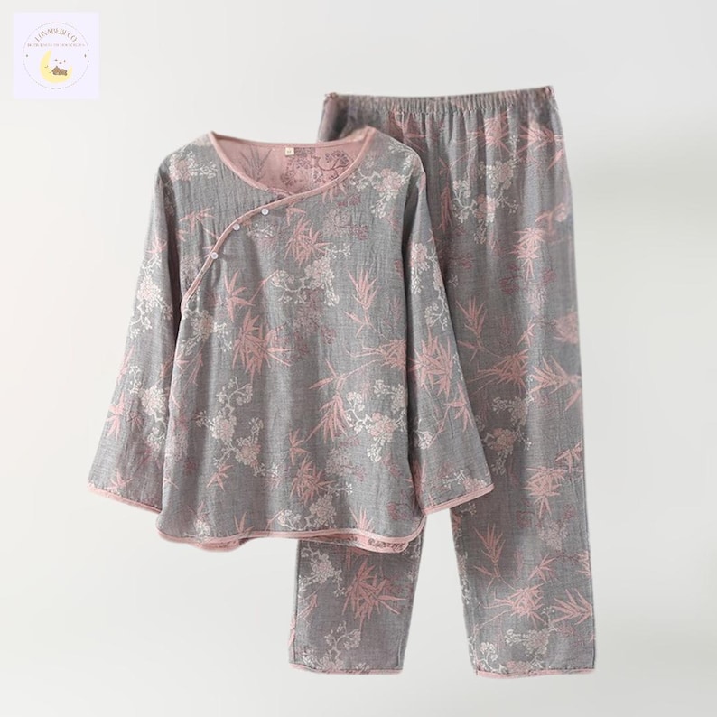 May include: Gray pajama set with a floral pattern in pink and white. The long-sleeved top has a wrap-style closure with buttons. The pants have an elastic waistband. The edges of the top and pants are trimmed in pink.