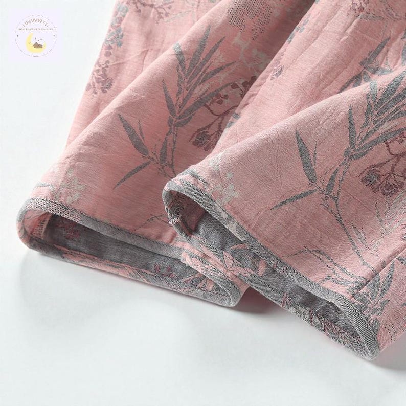 May include: Close-up of a pink fabric with a floral pattern in gray. The fabric is folded, revealing the gray lining and edges. The design features botanical elements, creating a soft, textured appearance.