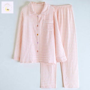 May include: A light pink and white checkered pajama set. The long-sleeved top has a button-down front, a chest pocket, and a white collar. The matching pants have an elastic waistband. The buttons are in different colors.
