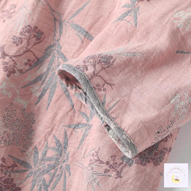 May include: Close-up of a pink fabric with a floral pattern in gray and purple. The sleeve of a garment is visible, with a gray trim along the edge. The fabric has a textured appearance.
