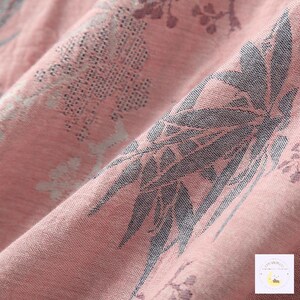 May include: Close-up of a pink fabric with a floral pattern. The fabric has a woven texture and features a design of gray leaves and flowers. The folds in the fabric create shadows and depth, highlighting the intricate details of the pattern.