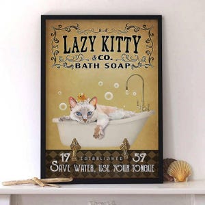 May include: A framed print featuring a cat relaxing in a bathtub filled with bubbles. The cat has blue eyes and wears a rubber ducky on its head. The print includes the text "LAZY KITTY & CO. BATH SOAP" and "SAVE WATER, USE YOUR TONGUE."