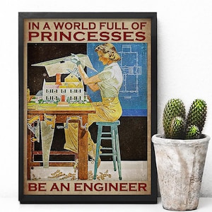 May include: Framed vintage-style poster with the text "IN A WORLD FULL OF PRINCESSES BE AN ENGINEER." The image depicts a woman working on a model house, with blueprints in the background. A cactus in a concrete pot is to the right.