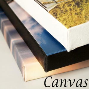Peut inclure: Gros plan sur trois impressions sur toile tendues. Les toiles pr&eacute;sentent des images d'un coucher de soleil, d'un ciel bleu avec des nuages et d'un paysage. Les bords sont noirs, blancs et bleus. Le mot "Canvas" est &eacute;crit en script noir.