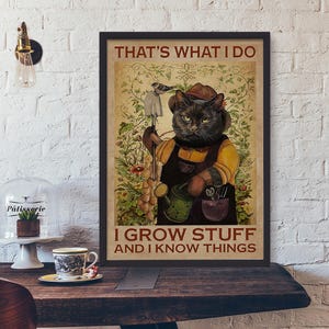 May include: Framed poster featuring a black cat dressed as a gardener, holding tools and a watering can. The poster reads "THAT'S WHAT I DO I GROW STUFF AND I KNOW THINGS" in a vintage style.
