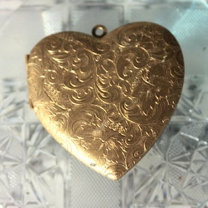 May include: A gold heart-shaped locket with an intricate floral pattern.