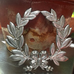 Pode incluir: Coroa de metal prateada com um laço no centro. A coroa é feita de folhas e bagas.