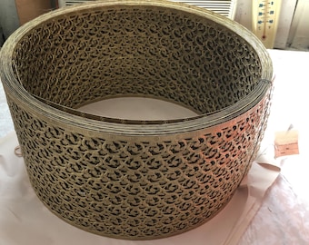 May include: A gold metal decorative trim with a repeating pattern of swirls and loops. The trim is rolled up in a circle.