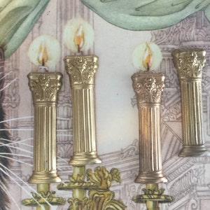 May include: Four gold-colored candle holders with ornate details and a flame-like design on top. The candle holders are arranged in a row on a patterned surface.