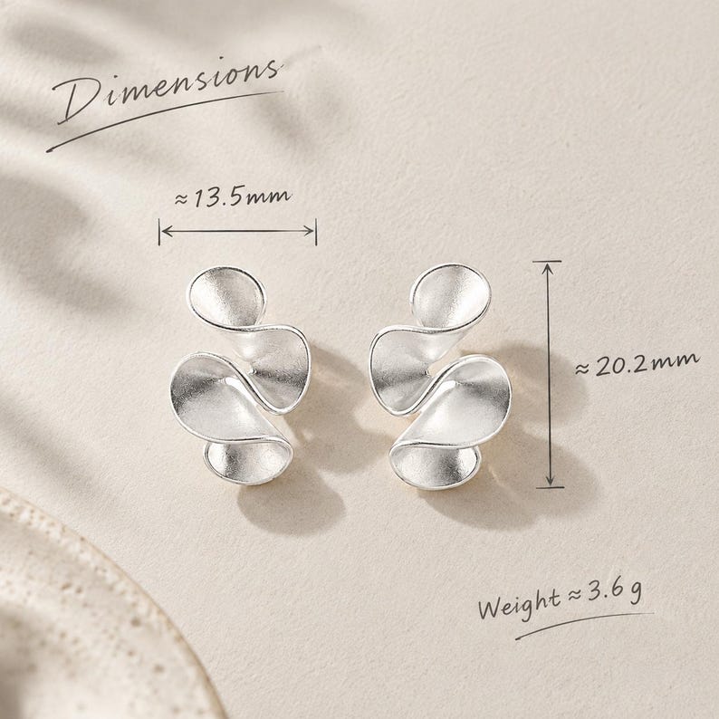 K&ouml;nnte beinhalten: Ein Paar silberfarbene Ohrringe mit geschwungenem, geschichtetem Bl&uuml;tendesign. Der Text Dimensions ist sichtbar und gibt eine Breite von ca. 13,5 mm und eine H&ouml;he von ca. 20,2 mm an. Das Gewicht wird mit ca. 3,6 g angegeben.