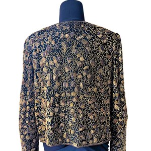 May include: A black jacket with intricate gold and brown beadwork. The jacket is displayed on a mannequin, showcasing the detailed pattern and design. The long sleeves and round neckline are visible.