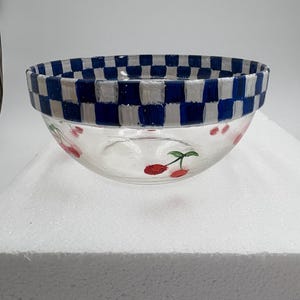 May include: A clear glass bowl with a blue and white chequered rim. The bowl features hand-painted red cherries with green stems. The bowl is a decorative kitchen item.