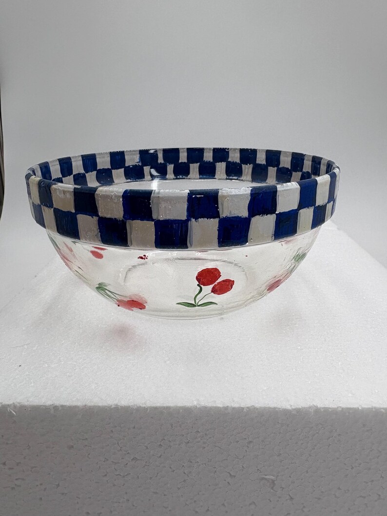 May include: A clear glass bowl with a blue and white chequered rim. The bowl features hand-painted red cherries on the sides. This decorative bowl is perfect for serving salads or displaying fruit.