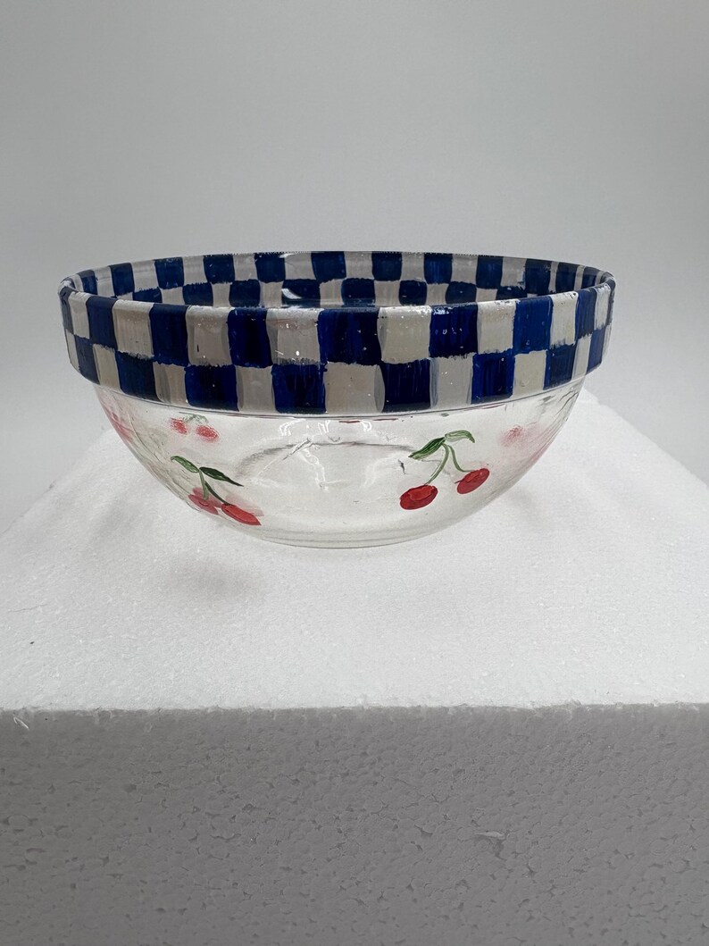May include: Clear glass bowl with a blue and white chequered rim. The bowl features hand-painted red cherries with green stems around the exterior. A decorative kitchenware item.