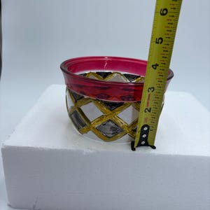 May include: A decorative glass bowl with a red rim and a geometric pattern of gold, black, and silver diamonds. The bowl is approximately 4 inches in diameter and 3 inches tall.