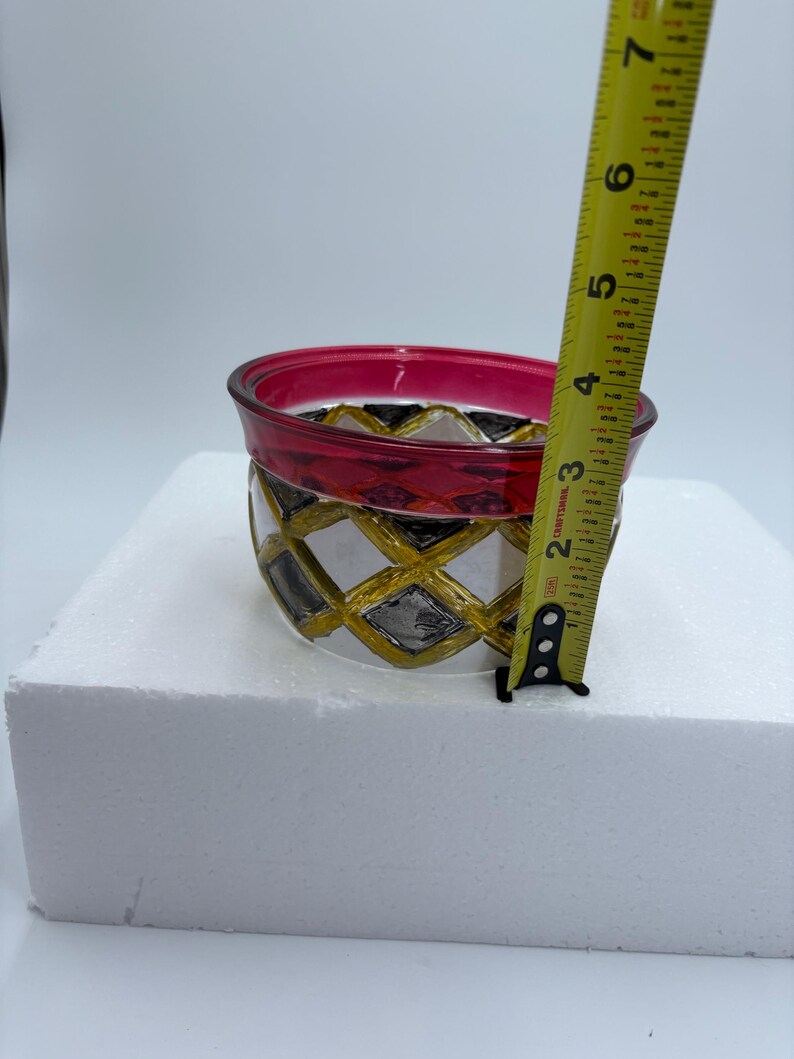 May include: A decorative glass bowl with a red rim and a geometric pattern of gold, black, and silver diamonds. The bowl is approximately 4 inches in diameter and 3 inches tall.