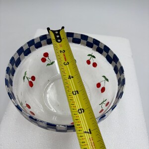 May include: A clear glass bowl with a blue and white checkered rim. The bowl is decorated with red cherries and green leaves. The bowl is approximately 18 cm in diameter.
