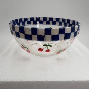 May include: A clear glass bowl with a blue and white chequered rim. The bowl features hand-painted red cherries with green stems around the base. This decorative bowl is perfect for serving snacks or displaying small items.