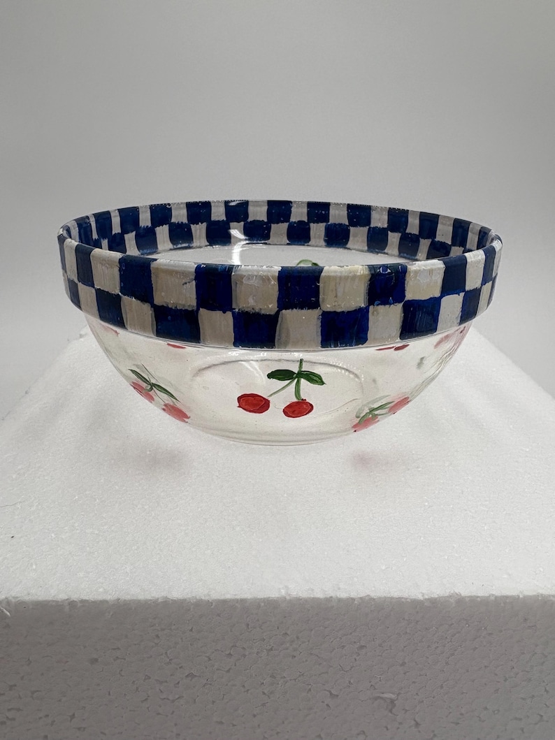 May include: A clear glass bowl with a blue and white chequered rim. The bowl features hand-painted red cherries with green stems around the base. This decorative bowl is perfect for serving snacks or displaying small items.