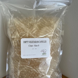 May include: A clear plastic bag filled with numerous clear, empty vegetarian capsules. The label reads "EMPTY VEGETARIAN CAPSULES Clear - Size 0". The quantity is 2000. The capsules are made of vegetable cellulose.