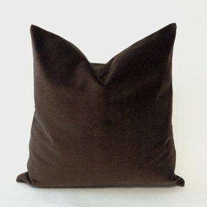 May include: A square, chocolate-brown velvet pillow. The pillow has a soft, plush appearance and a classic design. The pillow is a solid color and has a smooth texture. The pillow is a decorative item for a bed or sofa.
