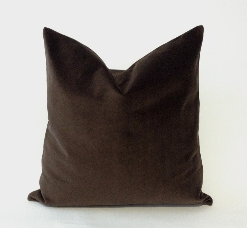 May include: A square, chocolate-brown velvet pillow. The pillow has a soft, plush appearance and a classic design. The pillow is a solid color and has a smooth texture. The pillow is a decorative item for a bed or sofa.