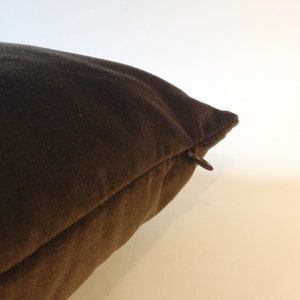 May include: Close-up of a brown pillow with a zipper closure. The pillow is a solid color and appears to be made of a soft fabric. The zipper is a dark brown color.