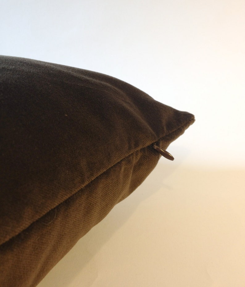 May include: Close-up of a brown pillow with a zipper closure. The pillow is a solid color and appears to be made of a soft fabric. The zipper is a dark brown color.