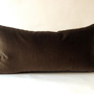 May include: A rectangular, brown velvet pillow. The pillow is a solid color and has a soft, plush appearance. The pillow is designed for decorative or functional use.