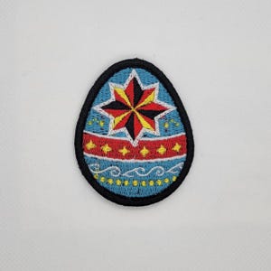Peut inclure: Écusson brodé en forme d'œuf, avec une étoile centrale rouge, jaune et noire. L'œuf a un fond bleu avec des accents rouges et jaunes, et une bordure noire. Idéal pour la décoration, il peut être cousu sur des vêtements.