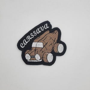 May include: Embroidered patch featuring a brown car design with white wheels and headlights. The patch has a black border and the word "CARSSAVA" in white, arched across the top. The patch is on a white background.