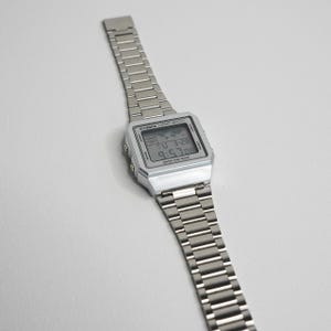 May include: A silver digital sport watch with a rectangular face and a metal band. The watch displays the time, date, and other functions on a digital screen. The watch is water resistant.