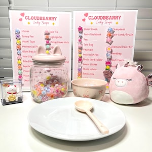 Puede incluir: Una exhibición de artículos Cloudbearry Lucky Scoops, que incluye un tarro rosa con tapa de orejas de gato, un cuenco pequeño, una cuchara, un peluche y una figura de gato de la suerte. El fondo presenta dos letreros rosas que enumeran varios artículos.