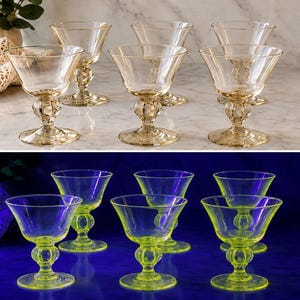 May include: A set of six clear, amber-tinted glass coupes with a wide bowl and a decorative, textured ball stem. The glass glows a vibrant, neon green colour when exposed to ultraviolet light, showcasing the unique properties of the material.