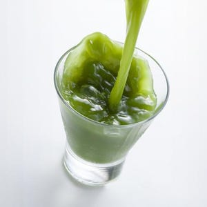 Puede incluir: Un vaso transparente que se está llenando con un líquido verde vibrante. El líquido se vierte en el centro del vaso, creando ondas y burbujas en la superficie. El vaso tiene una forma cónica y una base gruesa y sólida sobre un fondo blanco.