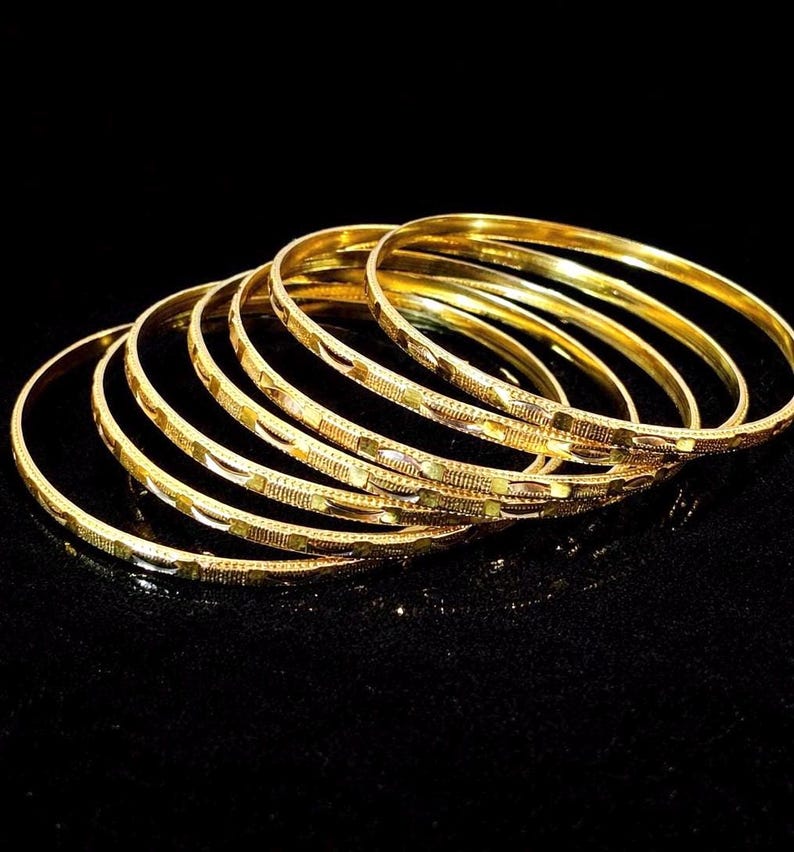 Peut inclure: Collection de bracelets dor&eacute;s avec des motifs grav&eacute;s complexes. Les bracelets sont empil&eacute;s, refl&eacute;tant la lumi&egrave;re sur un fond noir. Les bijoux sont en m&eacute;tal jaune brillant.