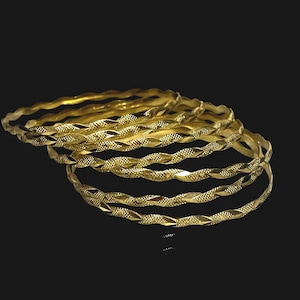 May include: A collection of six gold-colored bangles with a twisted rope design. Each bangle has a textured surface with a repeating pattern. The bangles are stacked and arranged against a black background.