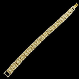 May include: A gold-colored bracelet with a textured, rectangular link design. The bracelet is shown against a black background, highlighting its intricate details and the warm tone of the metal. The clasp is visible at the end.