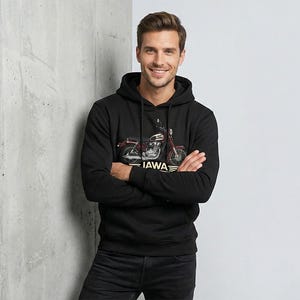 May include: Black hooded sweatshirt featuring a motorcycle graphic with the text "JAWA". The motorcycle is red and silver. The person is wearing black jeans and has their arms crossed.