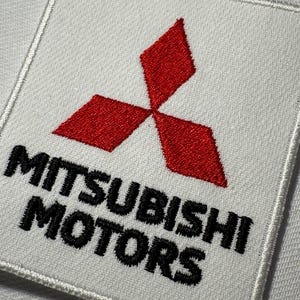 Könnte beinhalten: Ein quadratischer, weißer, bestickter Aufnäher mit dem roten Drei-Diamanten-Logo von Mitsubishi Motors in der Mitte oben, wobei der schwarze Text MITSUBISHI MOTORS in einer fetten serifenlosen Schrift direkt unter dem roten Diamant-Emblem gestickt ist.