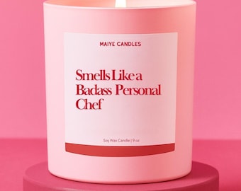 May include: A lit pink soy wax candle in a matching container, labeled "Smells Like a Badass Personal Chef." The candle is 9 oz and sits on a pink pedestal against a pink background. The brand name "Maiye Candles" is also visible.