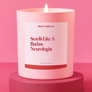 May include: A lit pink candle on a matching stand. The candle has a white label with the text "Smells Like A Badass Neurologist" in red. The candle is from Maiye Candles and is a 9 oz soy wax candle.