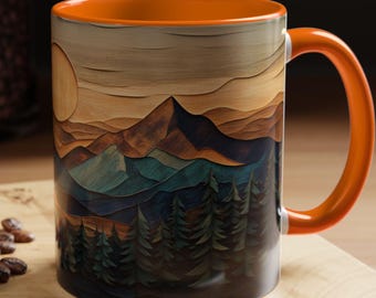 May include: A ceramic coffee mug with an orange handle and interior. The mug features a mountain landscape design in shades of brown, blue, and green, with a sun and trees. The mug is sitting on a wooden surface.
