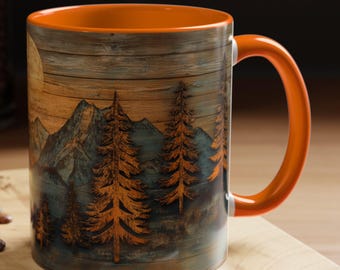 May include: A ceramic mug with an orange handle and interior. The exterior features a mountain and forest scene with a full moon. The mug is set on a wooden cutting board with a spoon and a macaron.