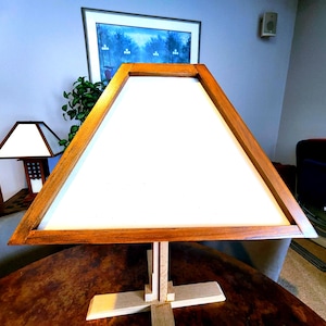 May include: A triangular wooden lamp with a white fabric shade. The lamp is sitting on a wooden table.